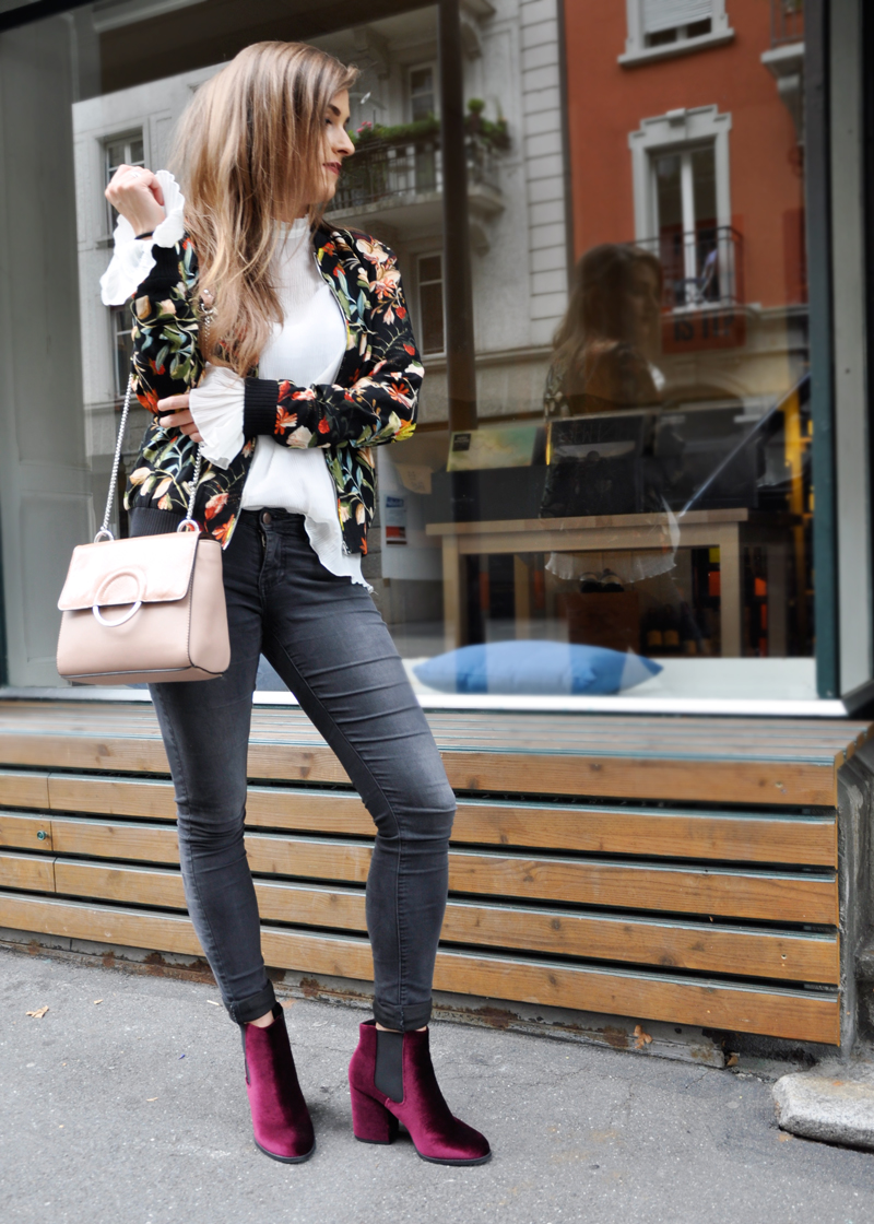 Skinny Jeans mit einer Rüschen-Bluse dazu eine Bomberjacke mit Blumenmuster von Zara und rote Samtschuhe von Zalando.