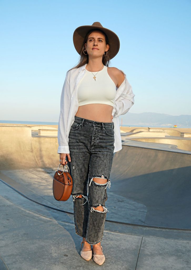 Andrea Steiner, fashion blogger von Strawberries 'n' Champagne trägt am Venice Beach eine schwarze Mom Jeans mit einem kurzen weissen Top und einer oversize Bluse