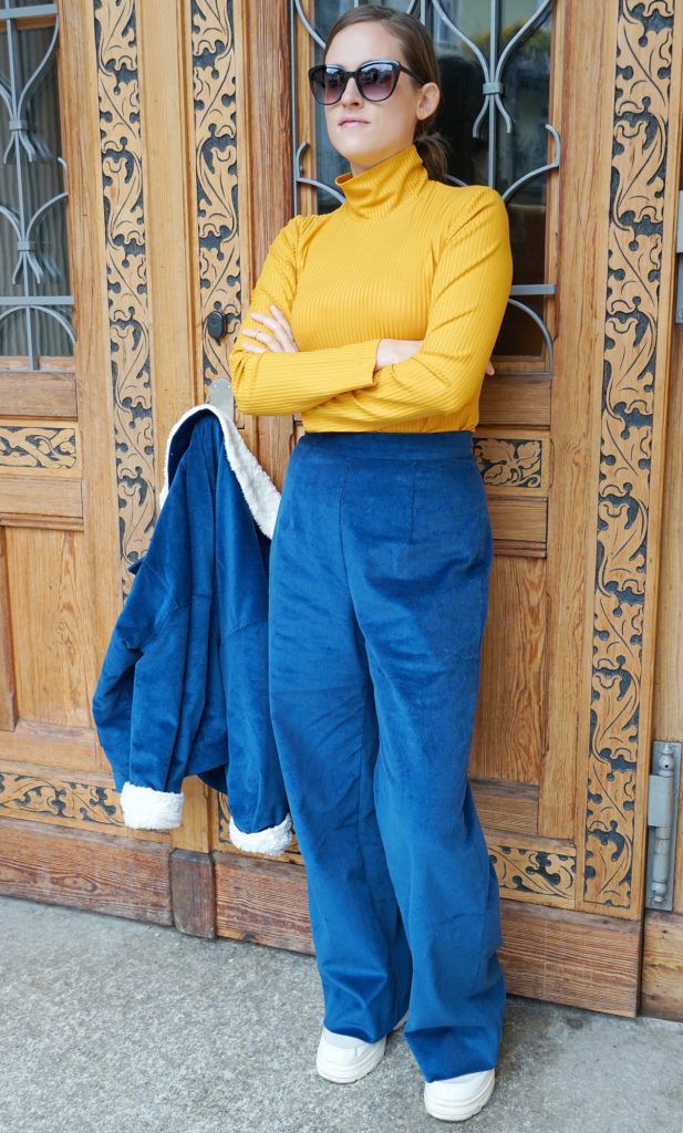 Andrea Steiner vom Mode Blog Strawberries 'n' Champagne aus der Schweiz trägt vegane und nachhaltige Mode. Einen blauen Anzug von SANIKAI, dazu einen gelben Pullover von JAN N JUNE und weisse Turnschuhe von EKIN.