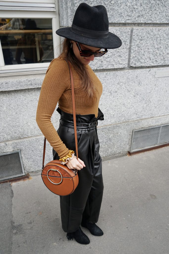 Andrea Steiner vom Mode Blog Strawberries 'n' Champagne aus der Schweiz trägt schwarze Lederhosen, einen braunen Rollkragen Pullover, dazu Tasche, Hut, Sonnenbrille und Plateauschuhe.